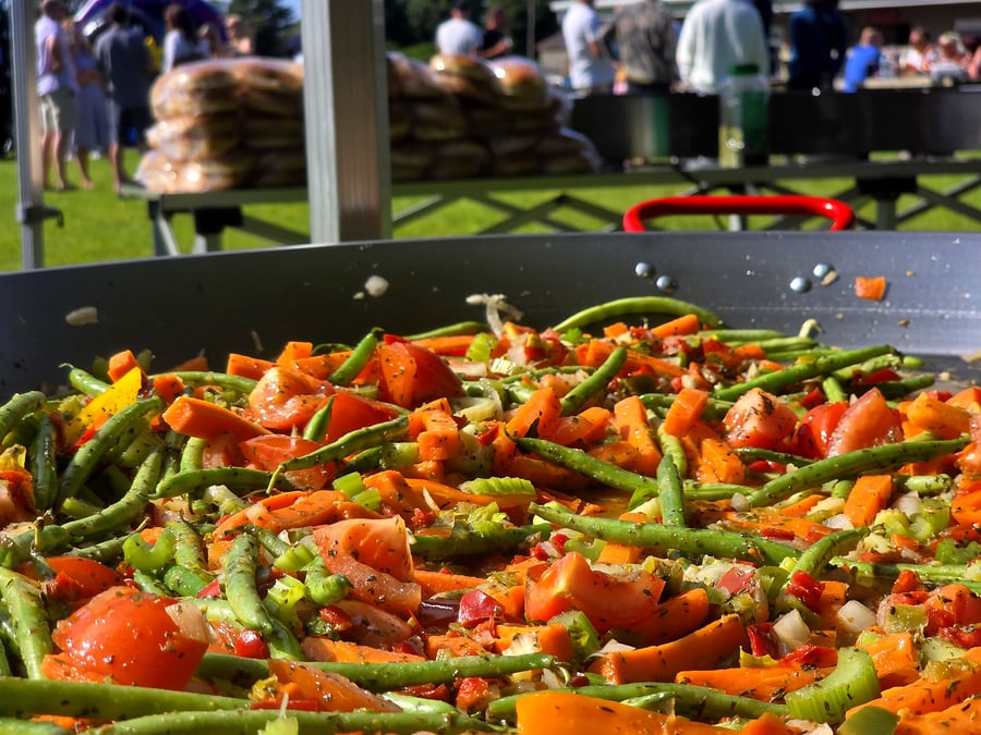 A large pan of colourful vegetables being cooked outdoors at an event