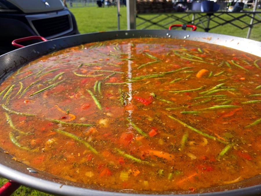 Giant pan of paella cooking outdoors with green beans and vegetables