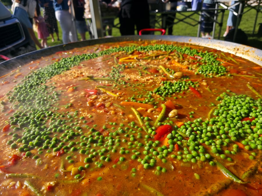 Giant pan of paella cooking outdoors with peas and vegetables