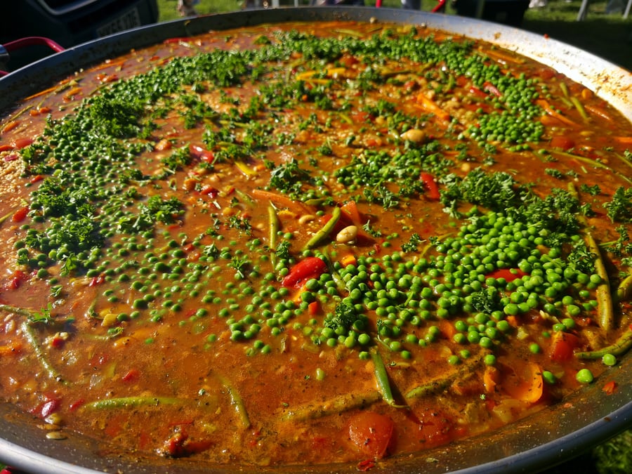 A giant pan filled with freshly cooked paella, garnished with peas and parsley