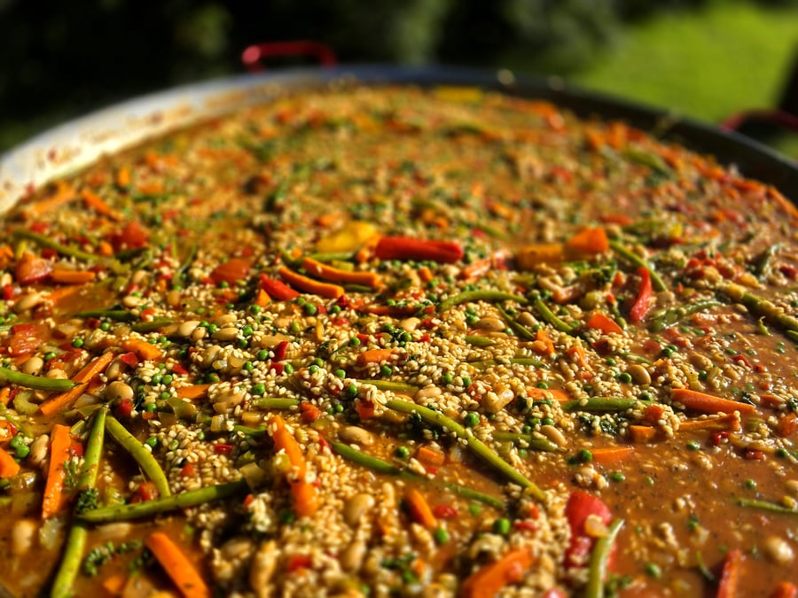A large pan of paella with vegetables and rice cooked outdoors