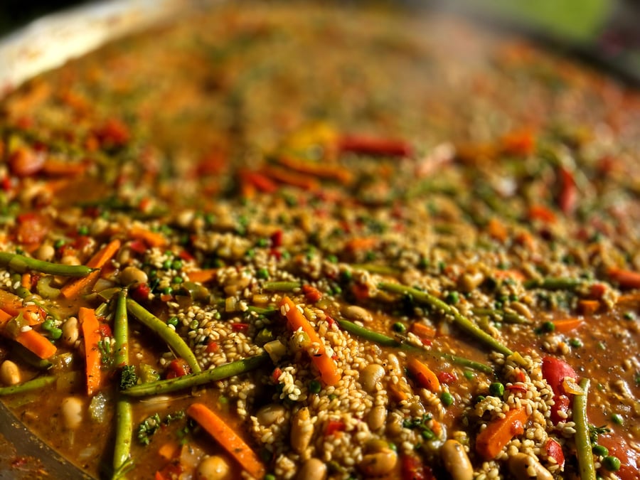 A large pan of paella with rice, beans, carrots, and green beans