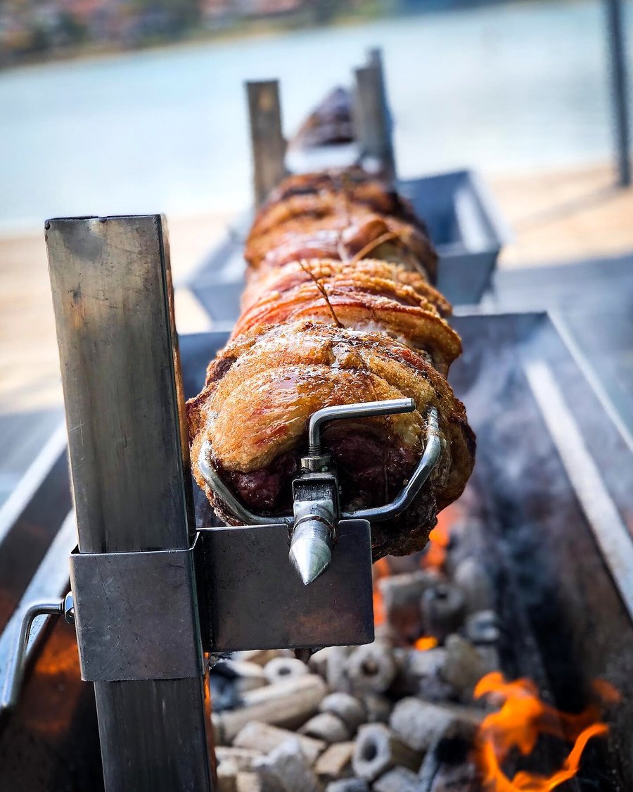 A whole hog is slowly roasting over glowing coals on a spit outdoors