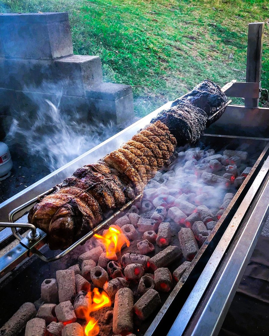 A large hog roast is slowly rotating over glowing coals and open flames