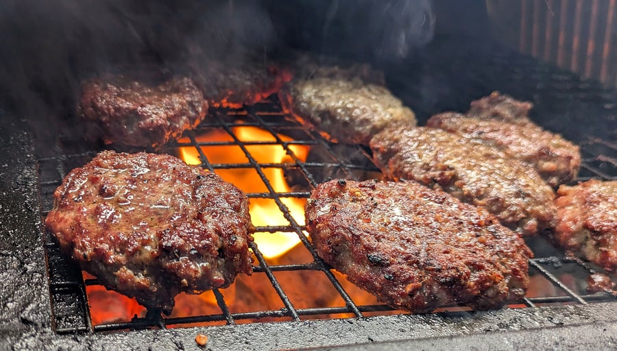 Juicy burgers sizzling on a hot grill with visible flames and smoke
