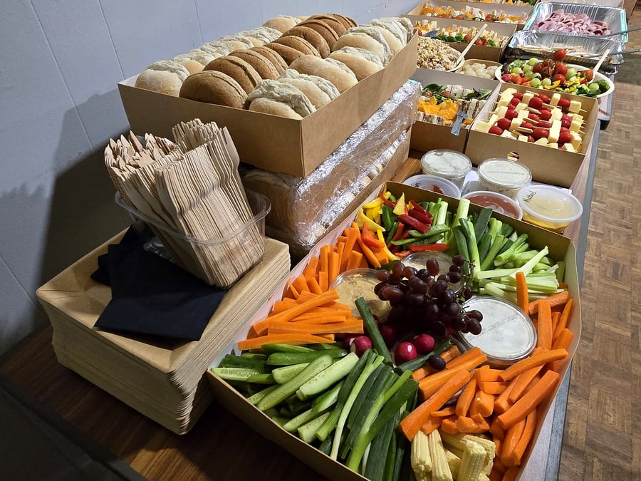 A long buffet table laden with sandwiches, crudités, dips, and fruit platters