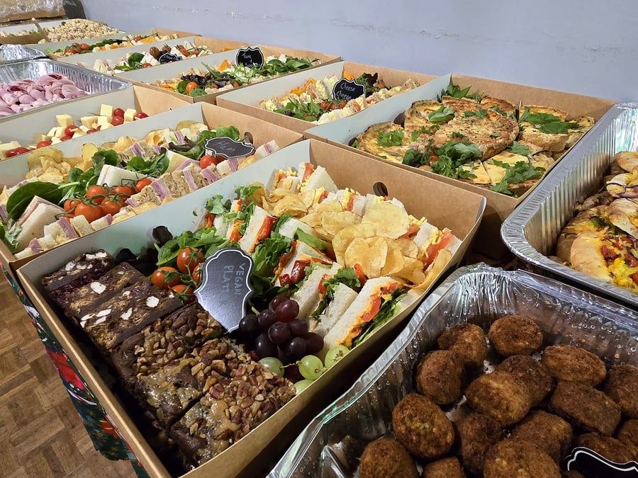 A long table laden with catering trays of sandwiches, quiches, brownies, and meatballs