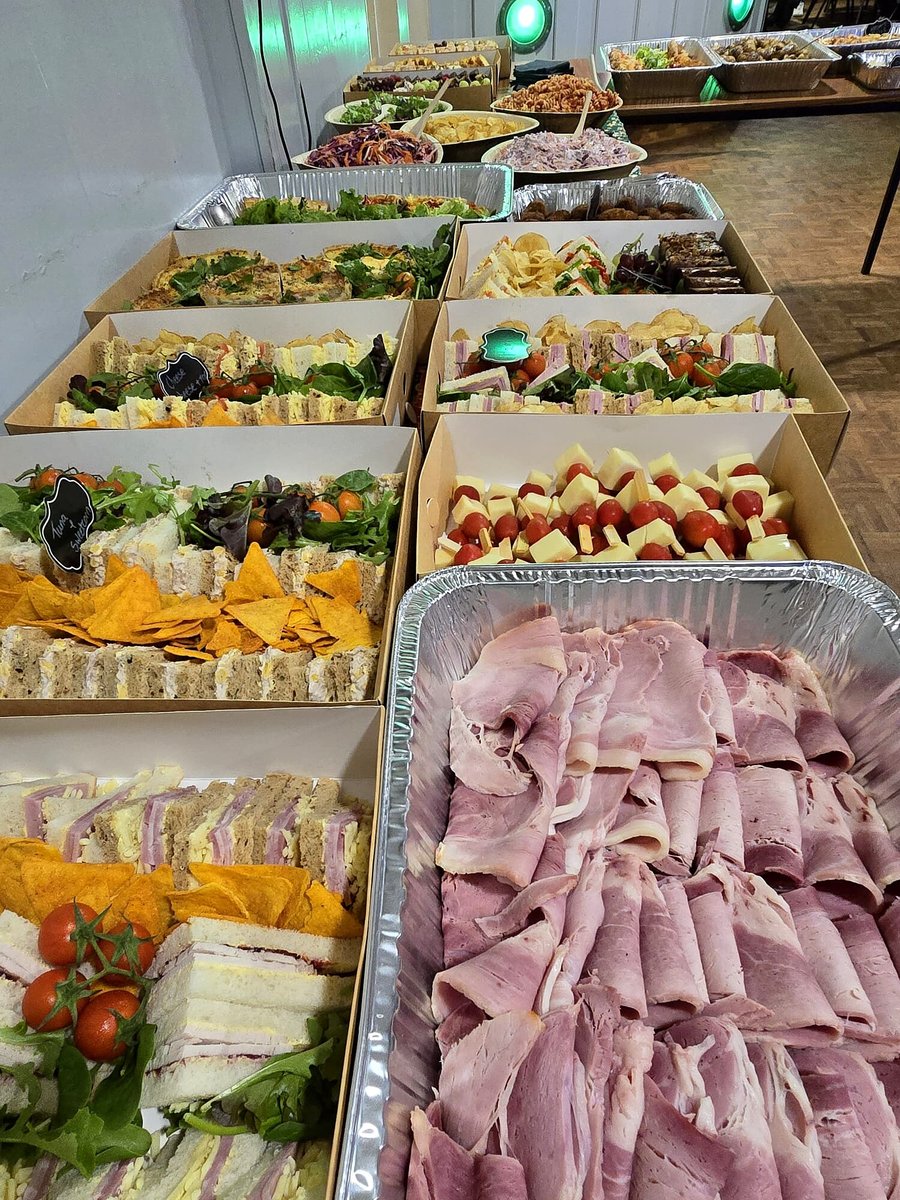 A long table laden with catering trays of sandwiches, salads, quiches, and ham