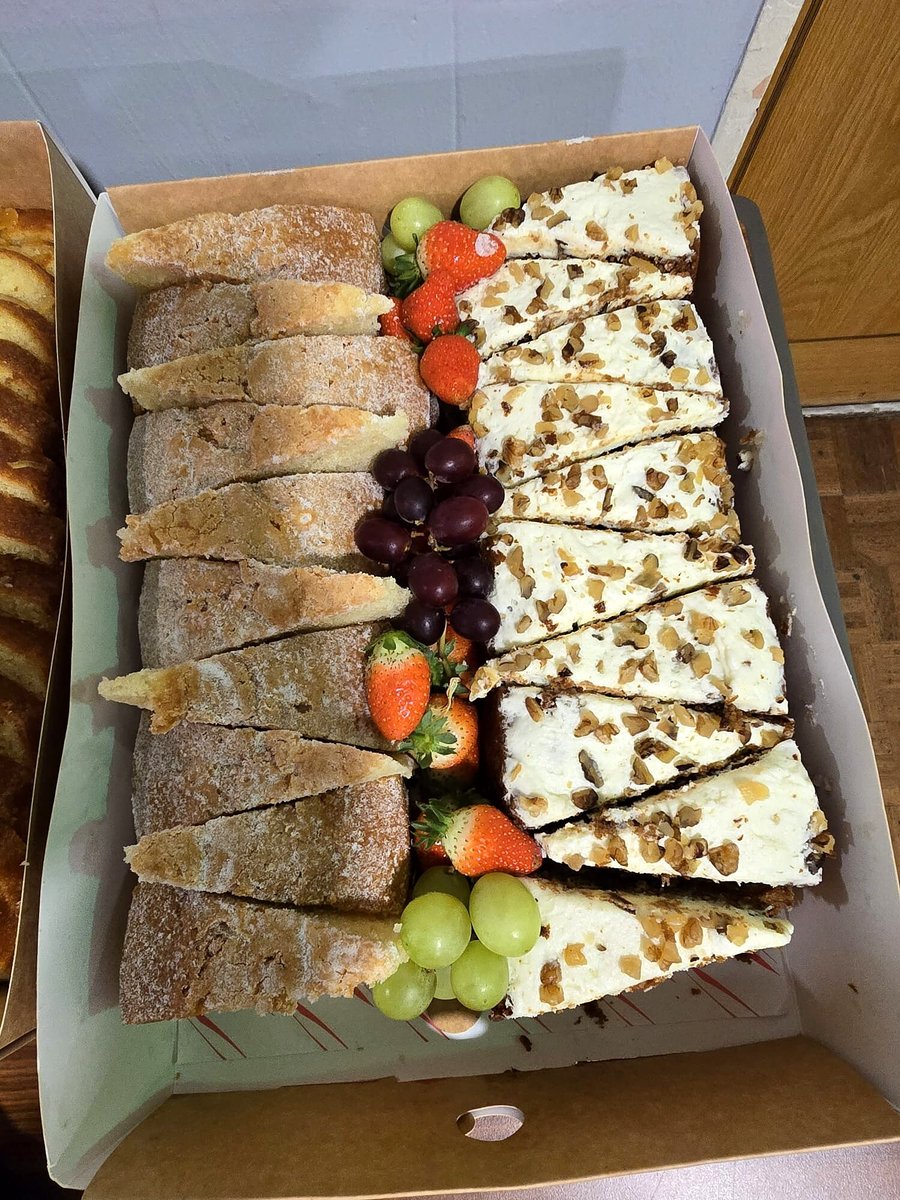 A platter of sliced cake, bread, strawberries, and grapes in a box