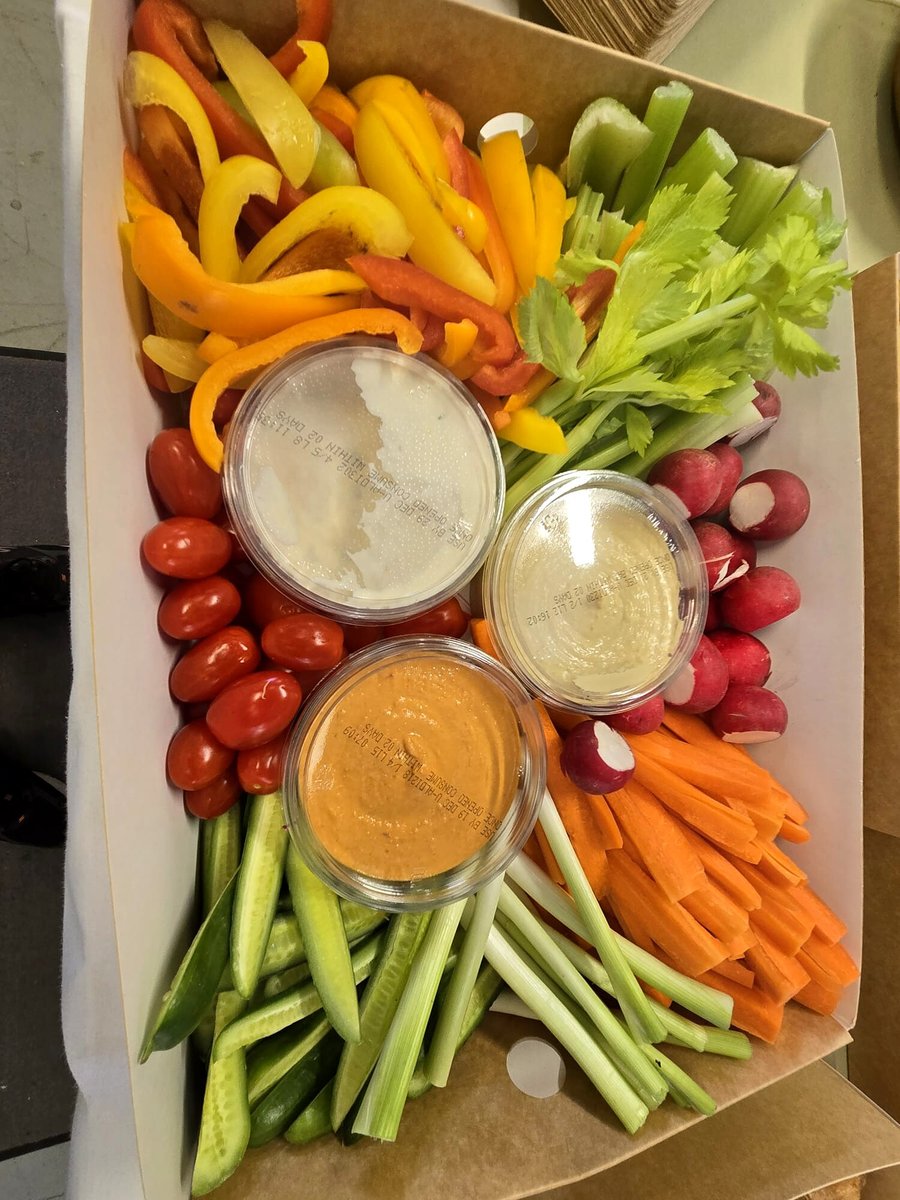 A platter of fresh crudités with three dips in a cardboard box
