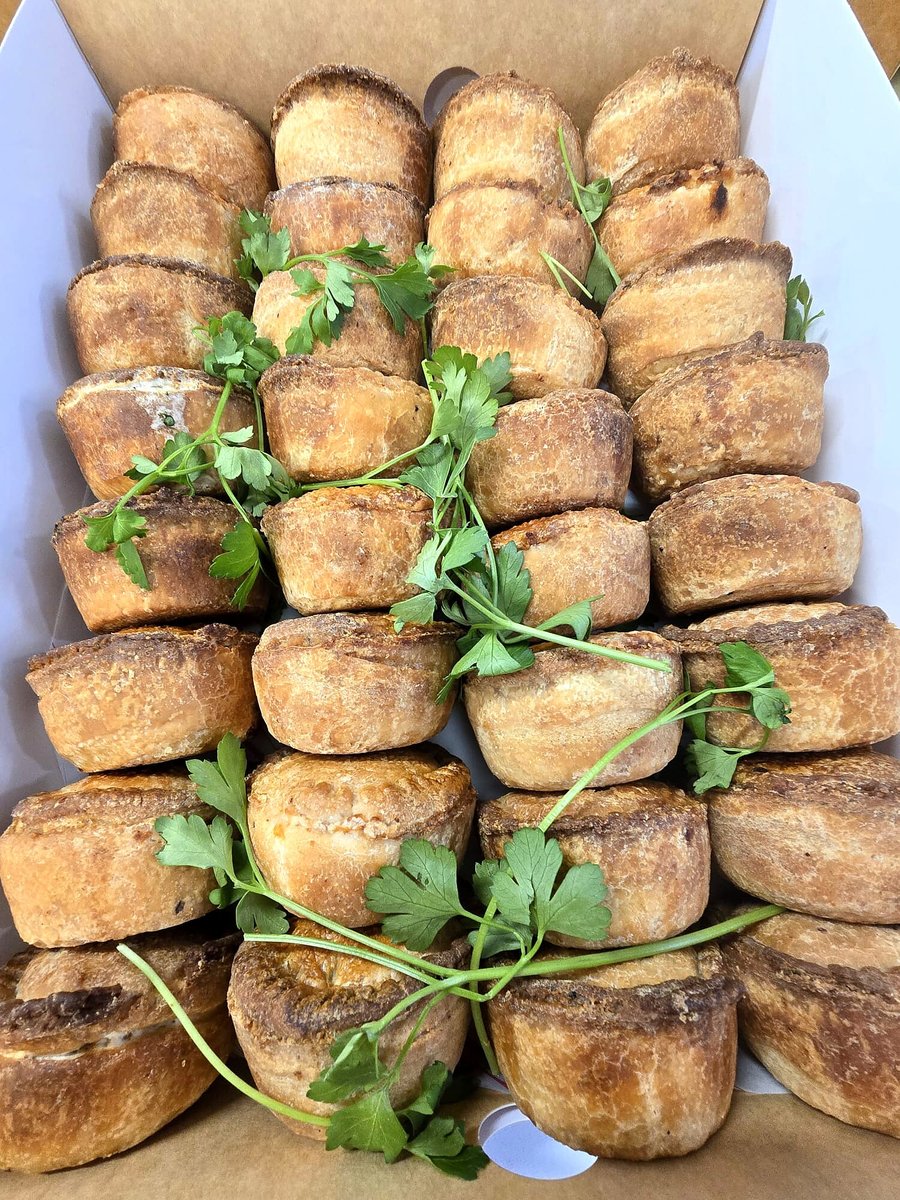 A box filled with golden-brown pies garnished with fresh parsley sprigs