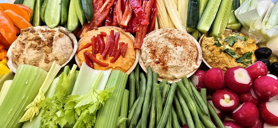 A vibrant platter of assorted hummus dips with fresh crudités and vegetables