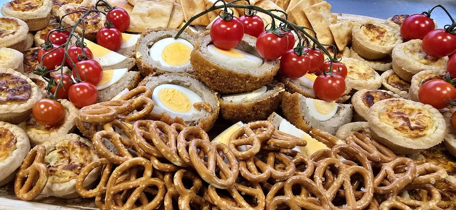 A close-up of a buffet platter featuring scotch eggs, mini quiches, pretzels, and tomatoes