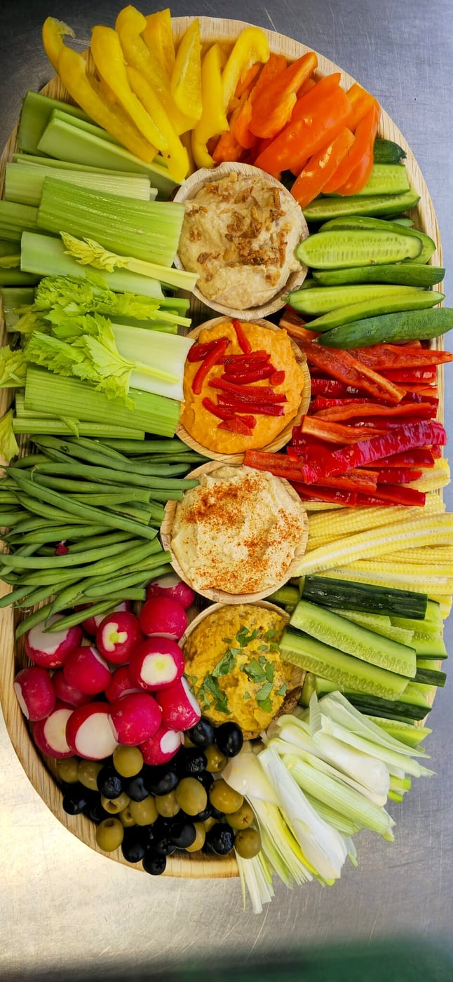 A large oval platter filled with colourful crudités, olives, radishes, and dips