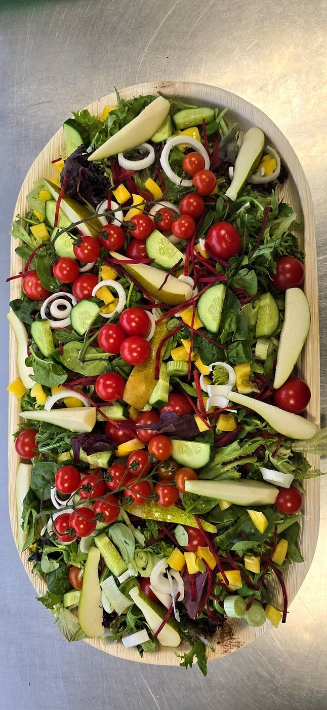 A large oval platter overflowing with a vibrant, fresh salad with cherry tomatoes and pear