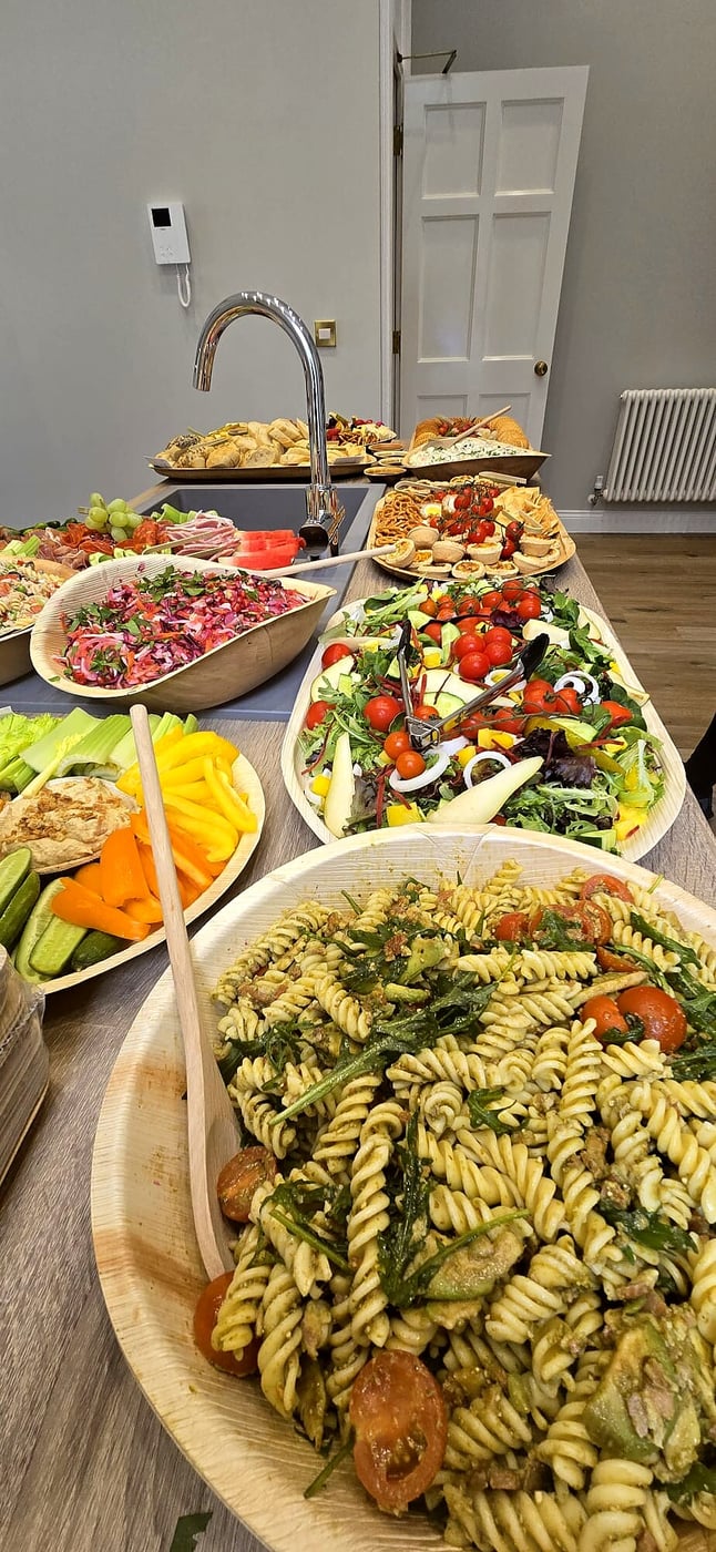 A long buffet table laden with various salads, pasta, and canapés