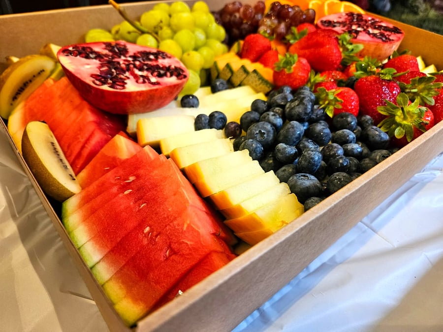 A close-up of a catering platter filled with fresh watermelon, strawberries, blueberries, and grapes