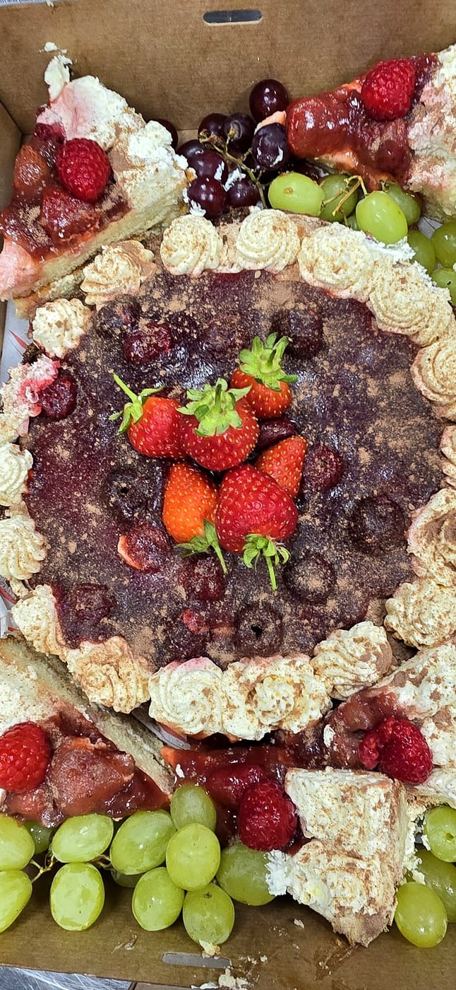 A close-up of a fruit tart with berries, grapes, and cream frosting