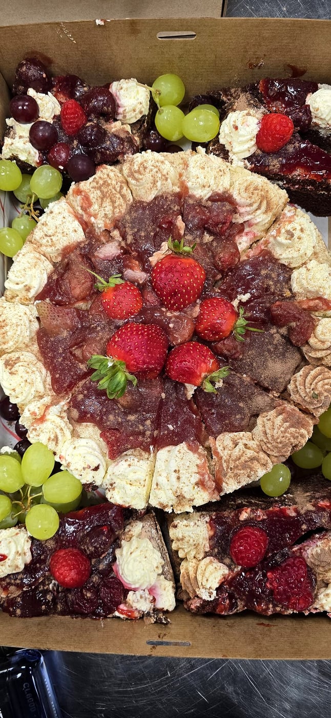A close-up of a decadent chocolate cake topped with strawberries, raspberries, and grapes