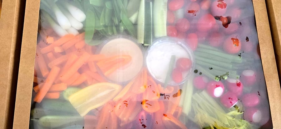 A platter of fresh crudités with two dips, presented in a cardboard box