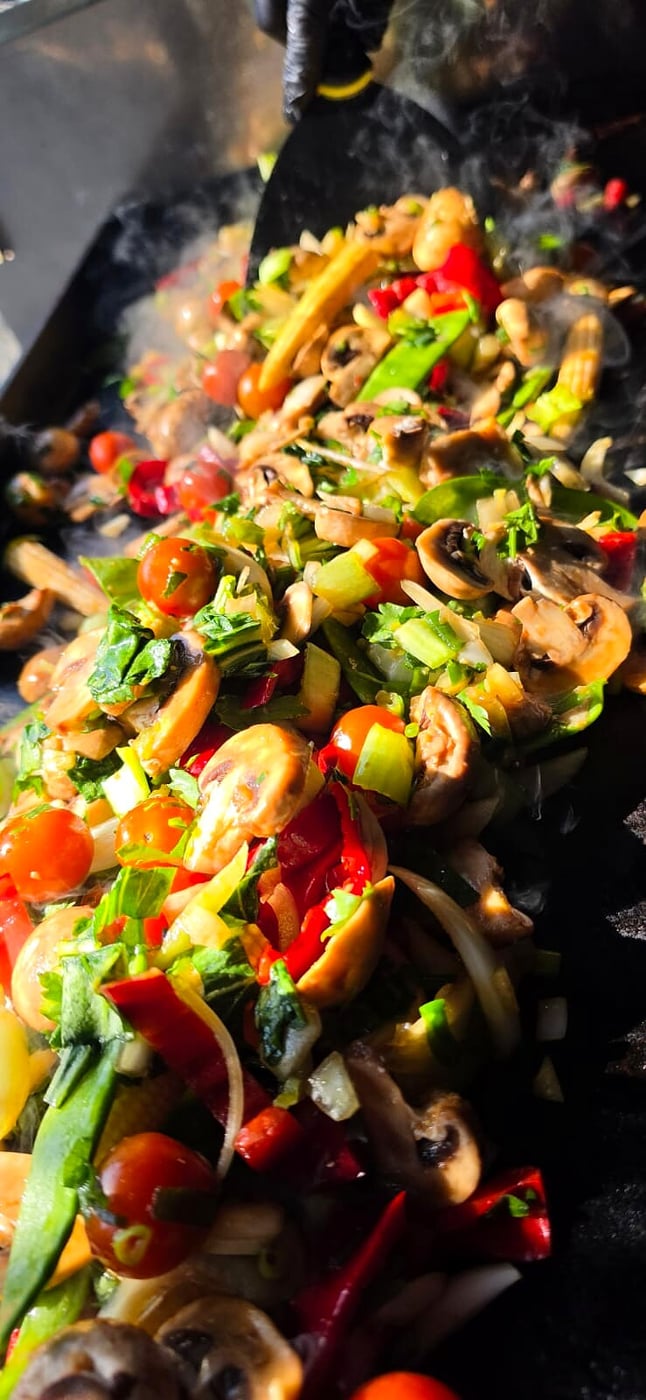 Fresh vegetables sizzling on a flat-top grill with visible steam and smoke