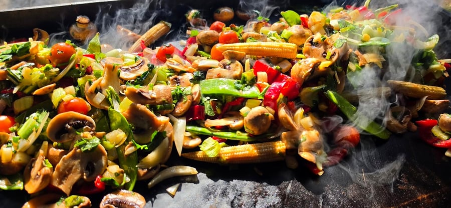Steaming hot vegetables and mushrooms cooking on a large flat-top grill