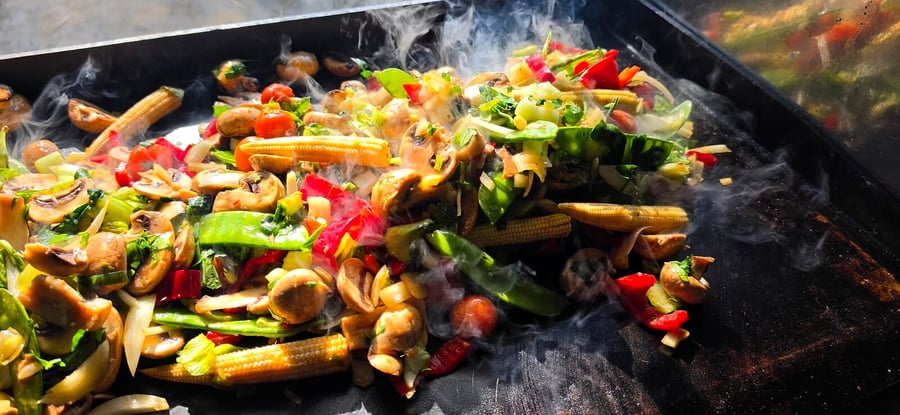 A vibrant mix of fresh vegetables sizzling on a hot grill with visible smoke