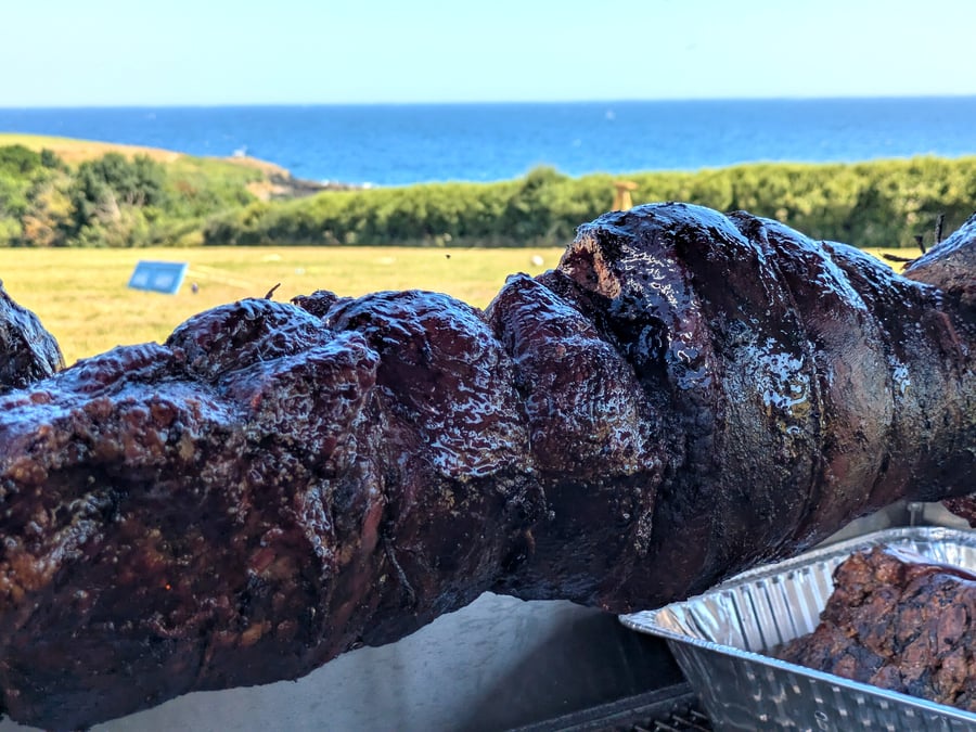 A hog roast is cooked outdoors with a beautiful coastal view in the background