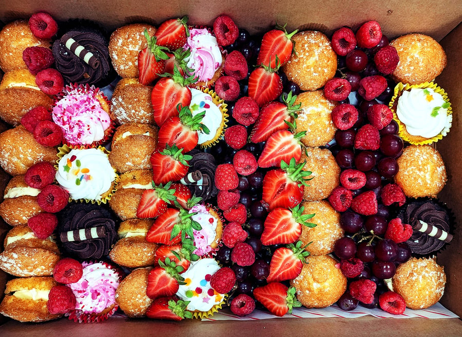 A box filled with assorted mini cupcakes and fresh berries, beautifully arranged