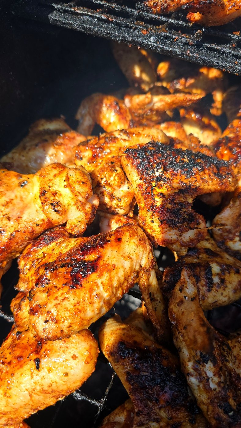 Close-up of delicious, seasoned chicken wings cooking on a smoky barbecue grill