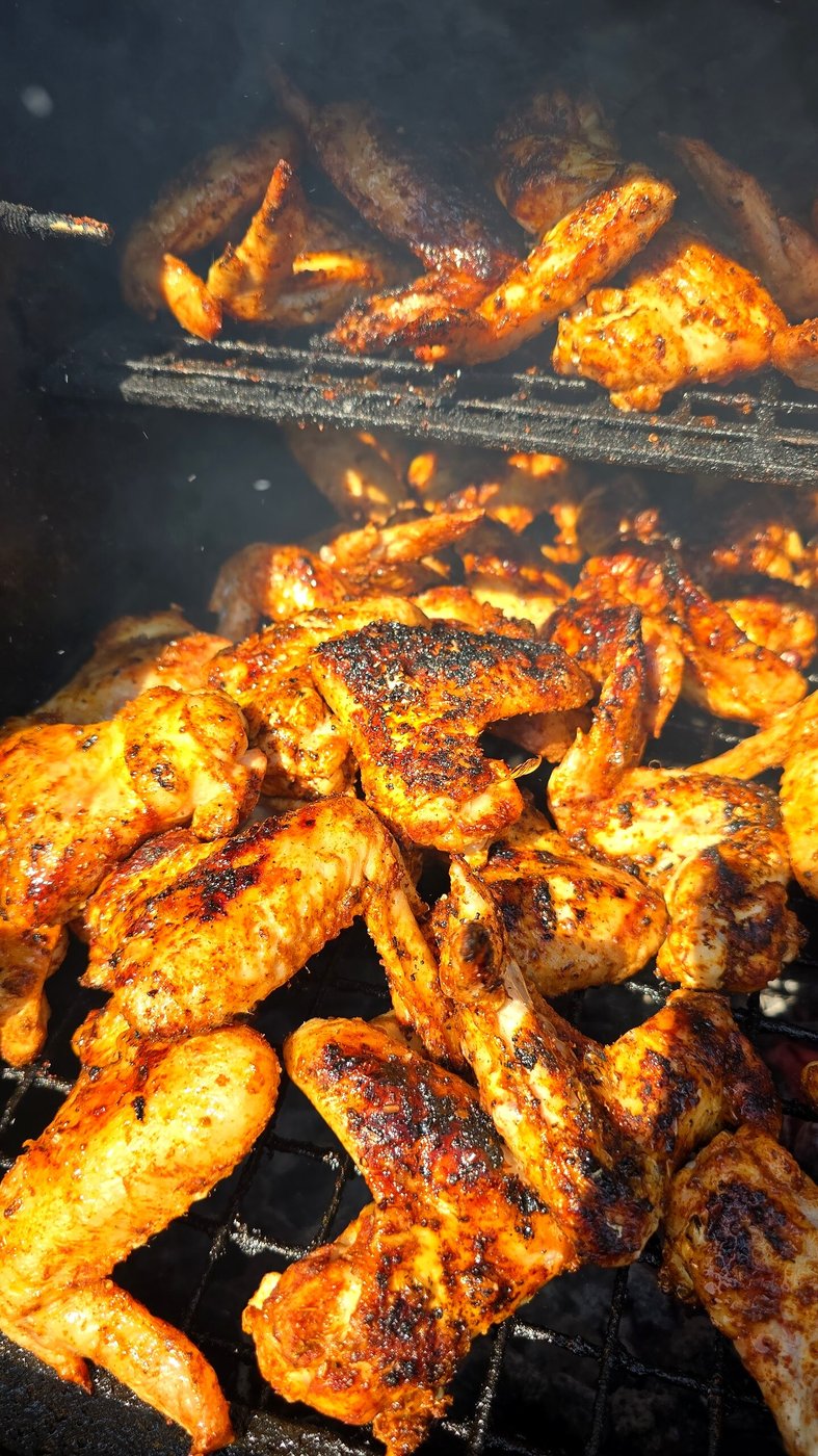 Juicy chicken wings cooking on a barbecue grill with visible smoke
