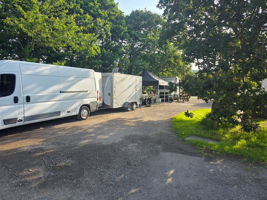 A white catering van and trailer parked at a film or TV production unit base, with a black gazebo set up in the background