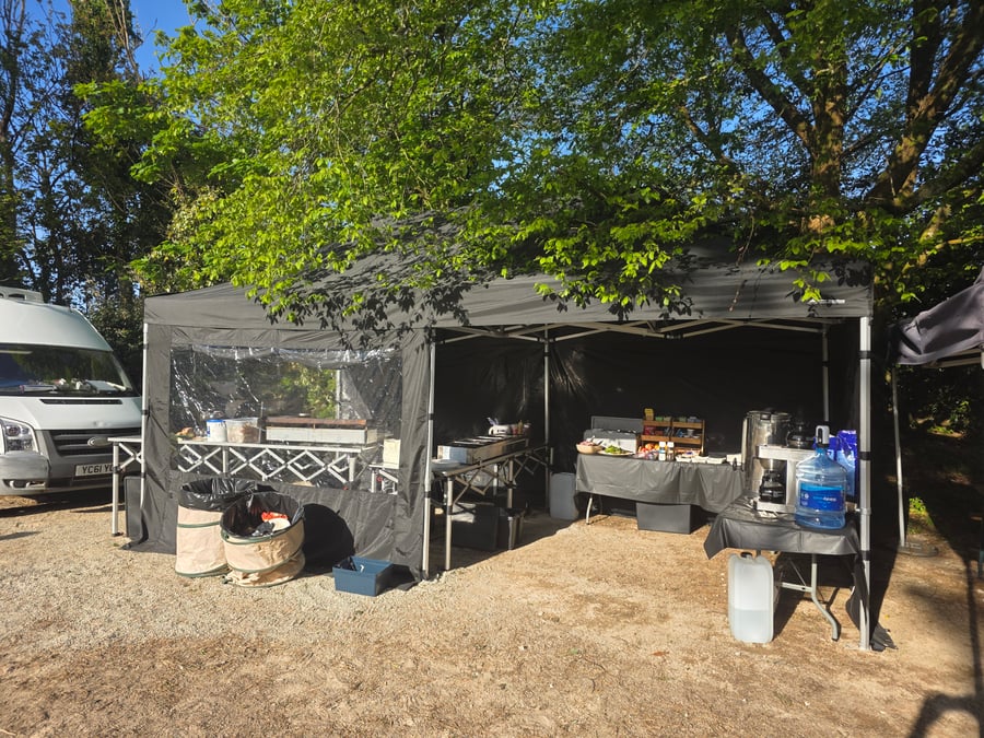 A catering setup under a gazebo at a film or TV production unit base, with a white van parked nearby