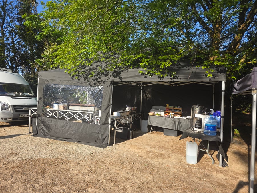 A catering tent with a buffet setup and a white van at a film or TV production unit base