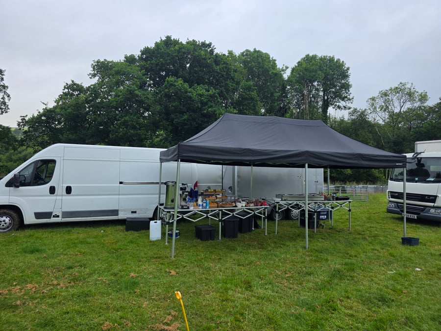A catering setup with a black gazebo, tables, and white vans in a grassy field, ready to serve a film or TV crew