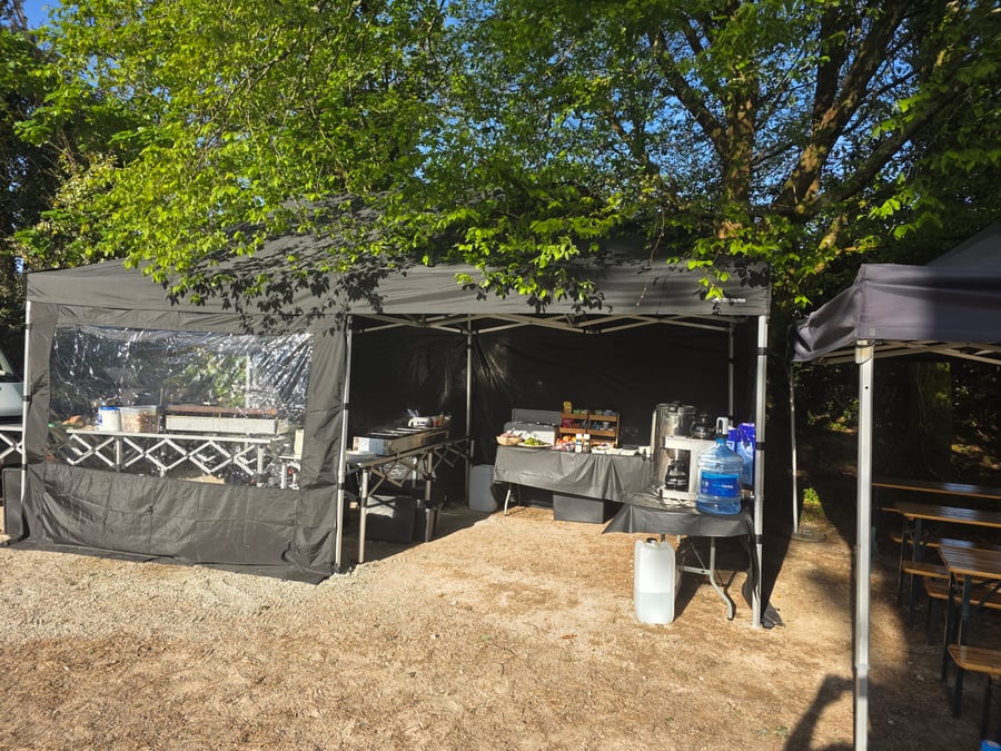 A catering setup with black gazebos and tables, ready for service under the shade of trees