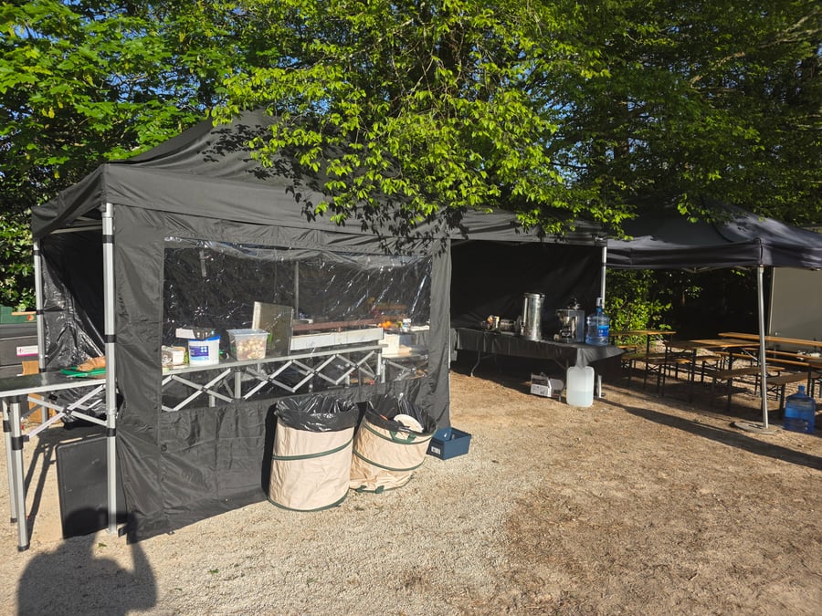 A catering gazebo with tables and equipment set up outdoors under trees, ready for an event