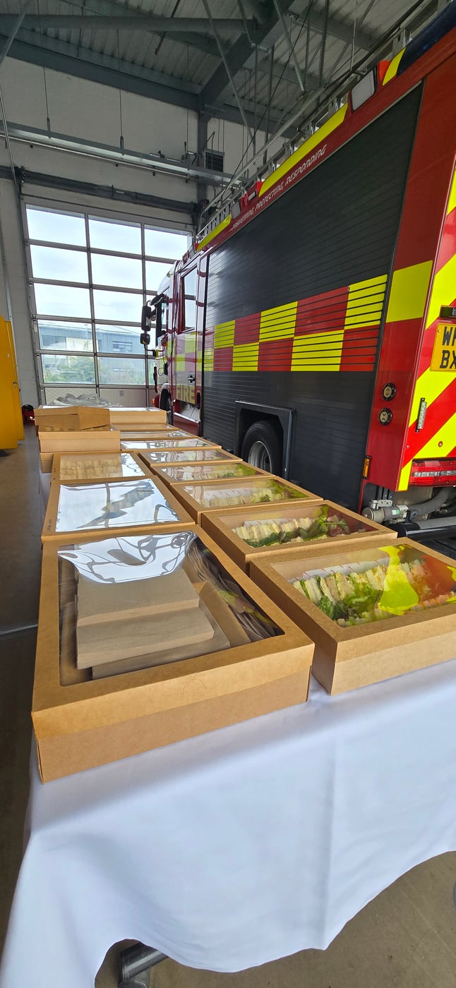 A table laden with individually packaged sandwiches and meals, set up in front of a fire engine, ready for welfare catering