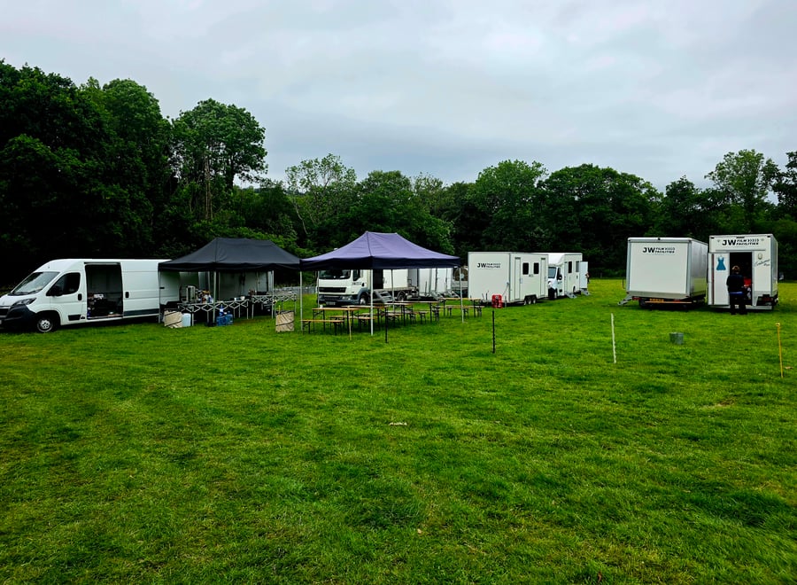 An outdoor catering setup with vans, marquees, and picnic tables on a grassy field, ready for an event in Cornwall