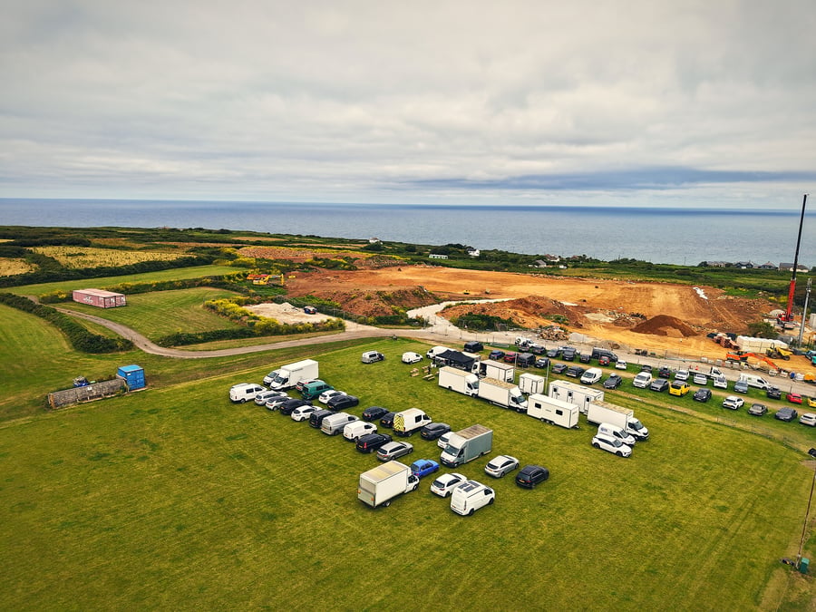 An aerial view of a film production unit base with vehicles and trailers on a grassy field by the coast