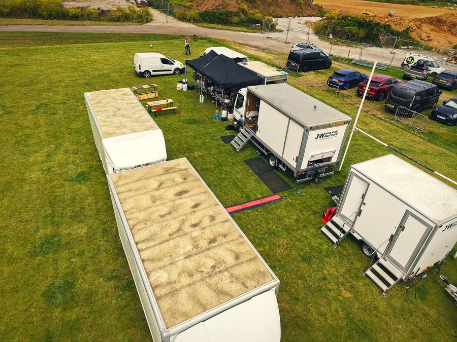 An aerial view of a film and TV production unit base with catering tents and vehicles set up on a grassy field