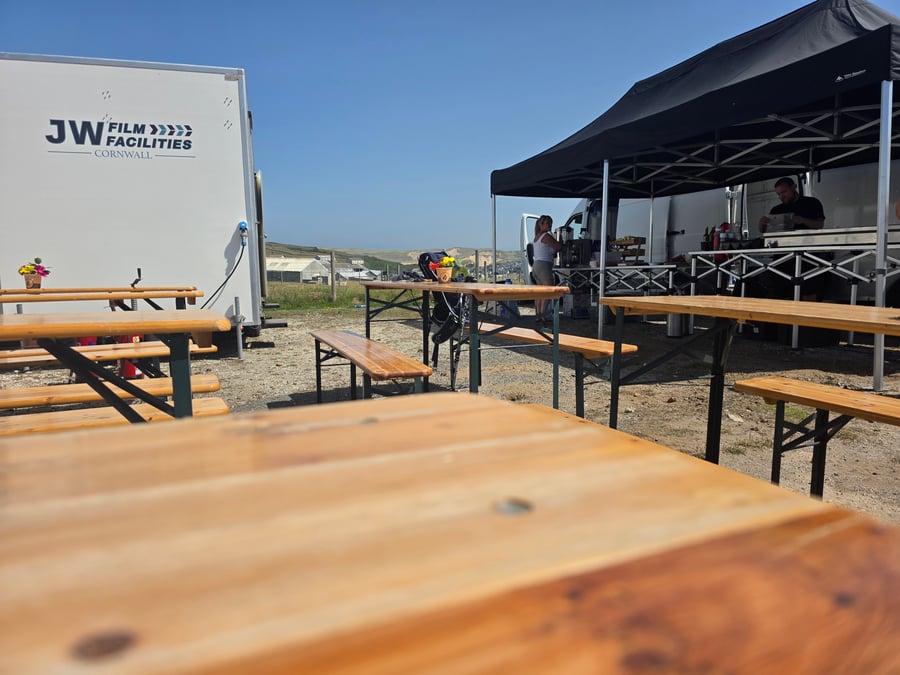 A film crew catering setup with outdoor tables and a branded production facility trailer under a clear blue sky