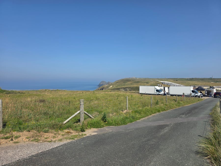 A film or TV production unit base with catering trucks and vehicles set up in a field overlooking the Cornish coast