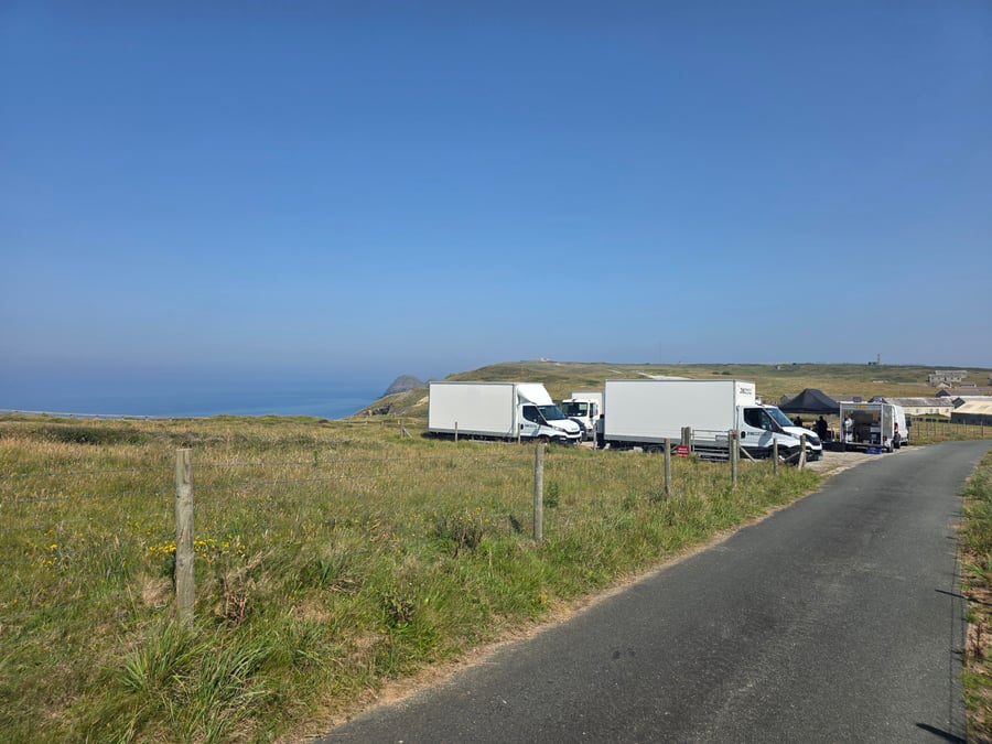 A film crew unit base with catering vans and marquees set up in a field overlooking the sea on a sunny day