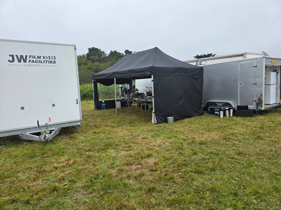 A catering tent and trailers are set up on a grassy field for a film and TV production unit base in Cornwall