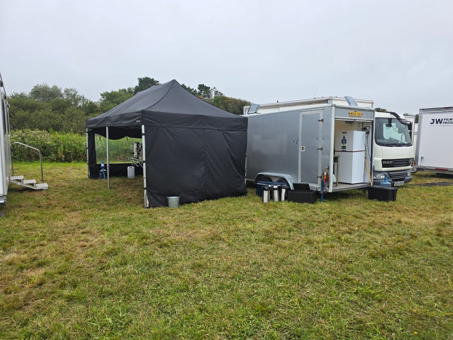 A black gazebo and catering trailer at a film or TV production unit base on a grassy field