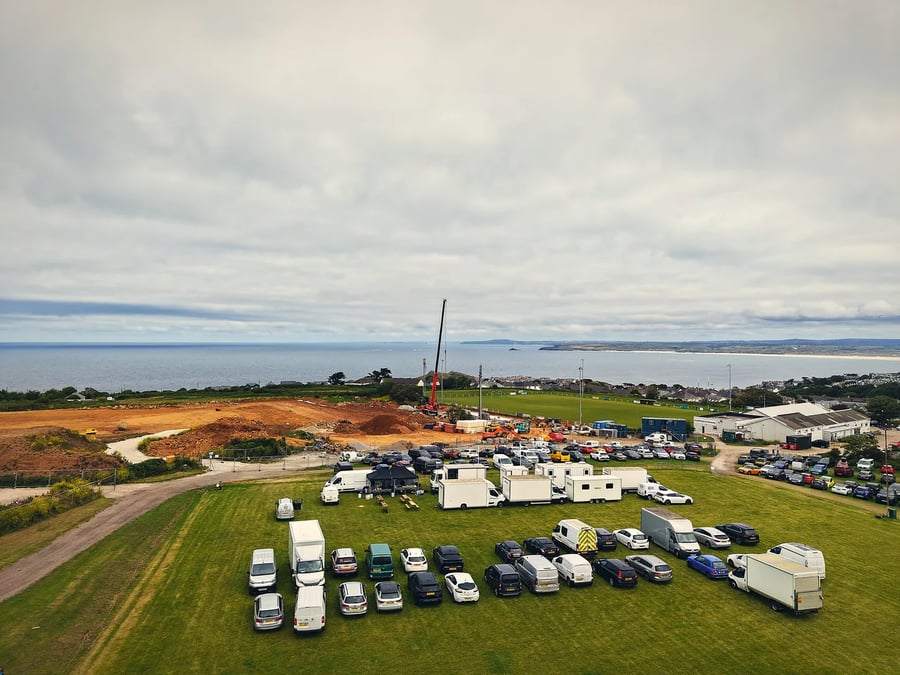 Aerial of a film unit base and crew car park overlooking the sea in Cornwall, set up for a production shoot