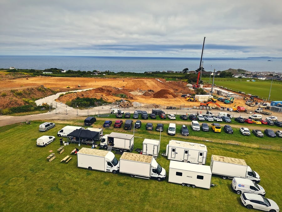 Aerial of a complete film unit base on the Cornwall coast, with the catering gazebo, box trucks and welfare trailers lined up above the sea