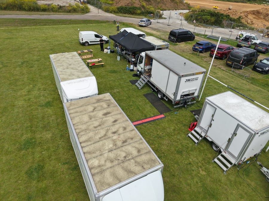 Close aerial of a film unit base in Cornwall — the catering setup alongside crew welfare trailers and cast-and-crew vehicles on location