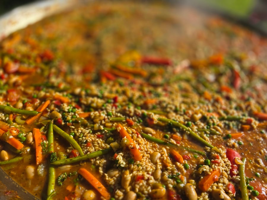 A vibrant giant paella pan filled with rice, beans, carrots, and green beans, steaming hot and ready to serve